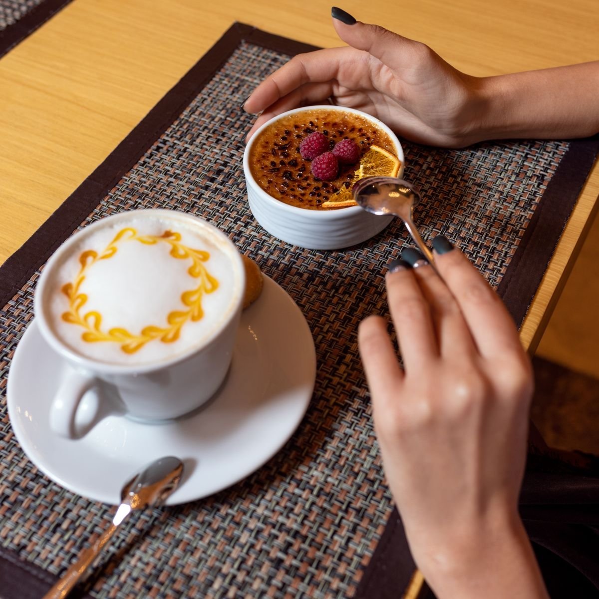 Une crème brûlée caramélisée aux framboises et un cappuccino avec dessin dans la mousse sur une table.
