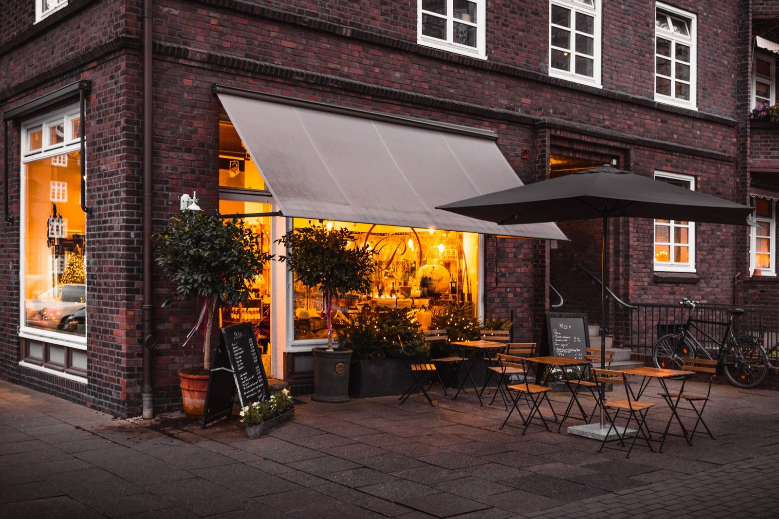 Devanture d'un café en soirée, fenêtres éclairées et terrasse.